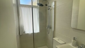Ett modernt badrum med en dusch som är avskärmad med glasväggar, en toalett och ett handfat med en spegel.