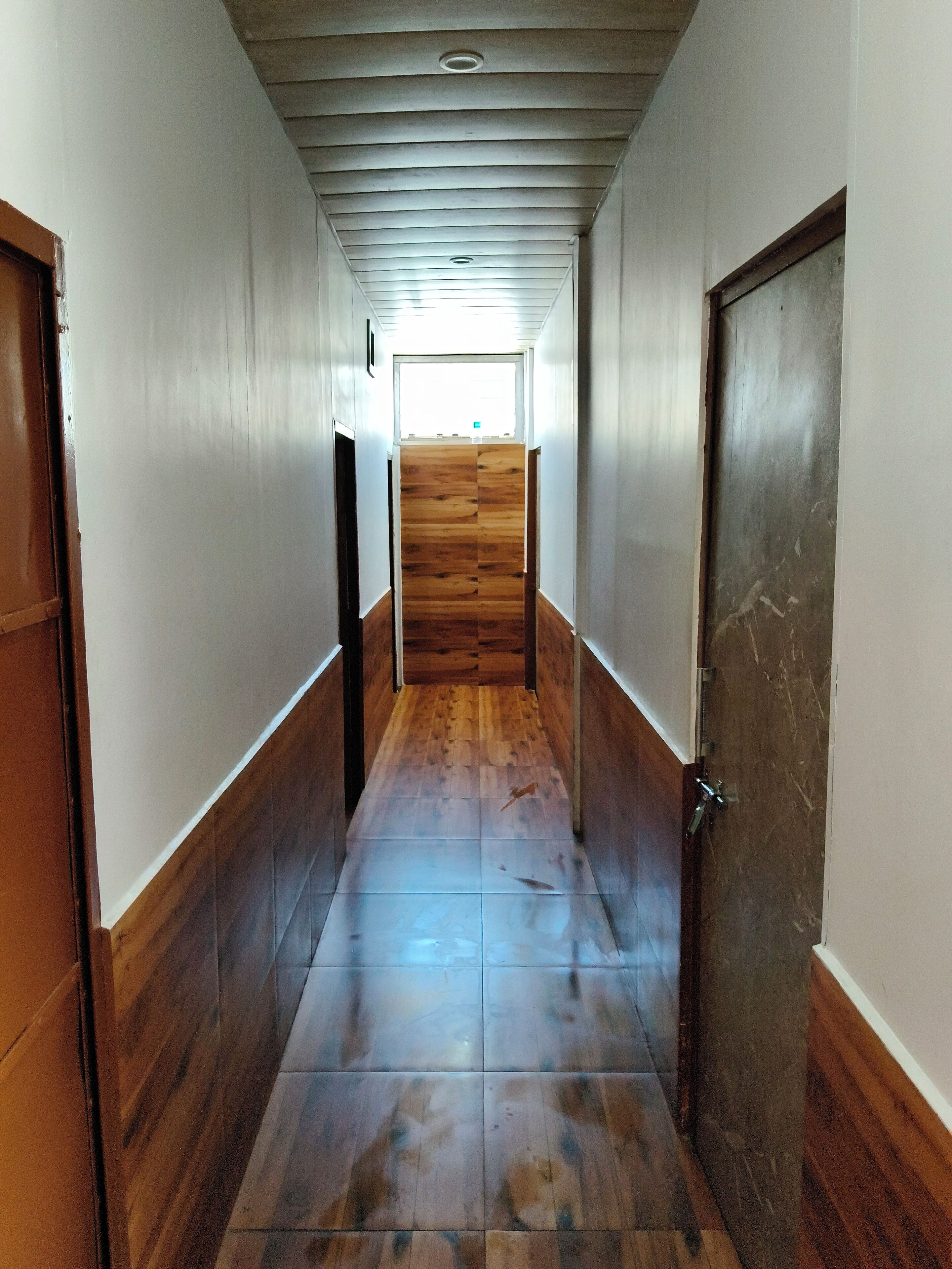 A hallway with wooden flooring and a tiled floor leading to a door.