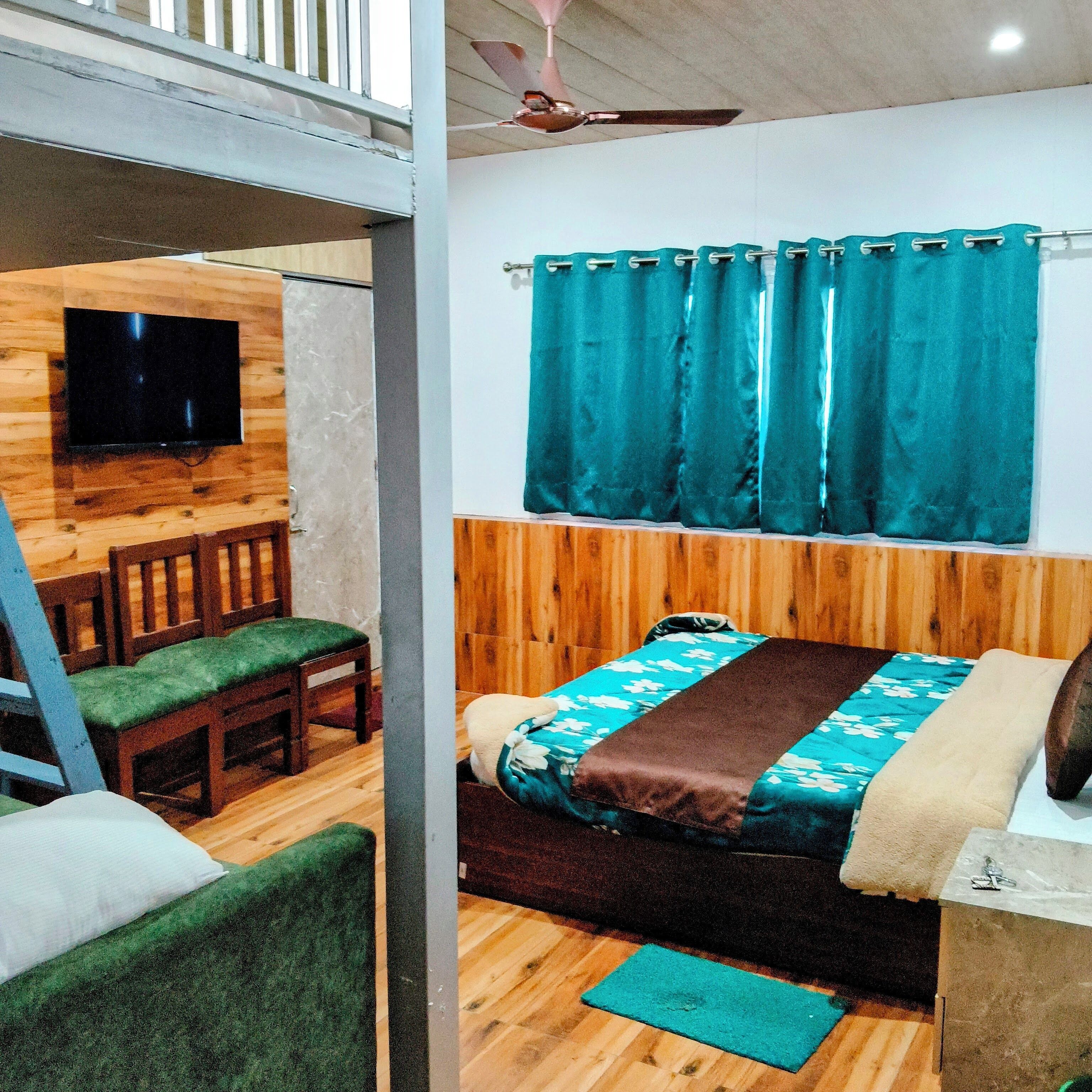 A room with a bed, a wooden headboard, a TV mounted on a wooden wall, a ceiling fan, and a window with teal curtains.