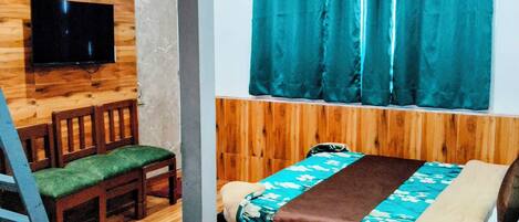 A room with a bed, a wooden headboard, a TV mounted on a wooden wall, a ceiling fan, and a window with teal curtains.