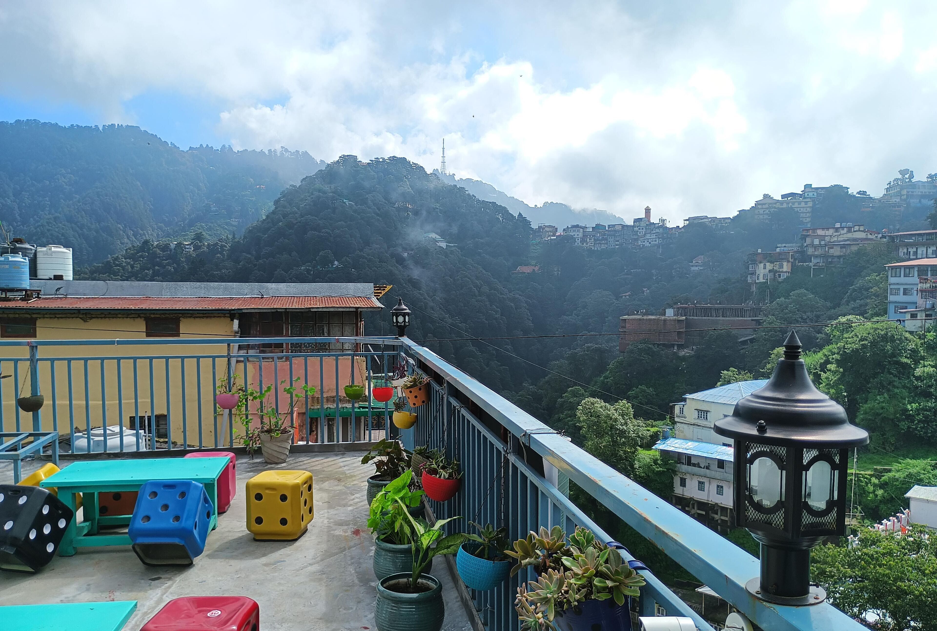 A balcony with potted plants, colorful stools, and a clock.