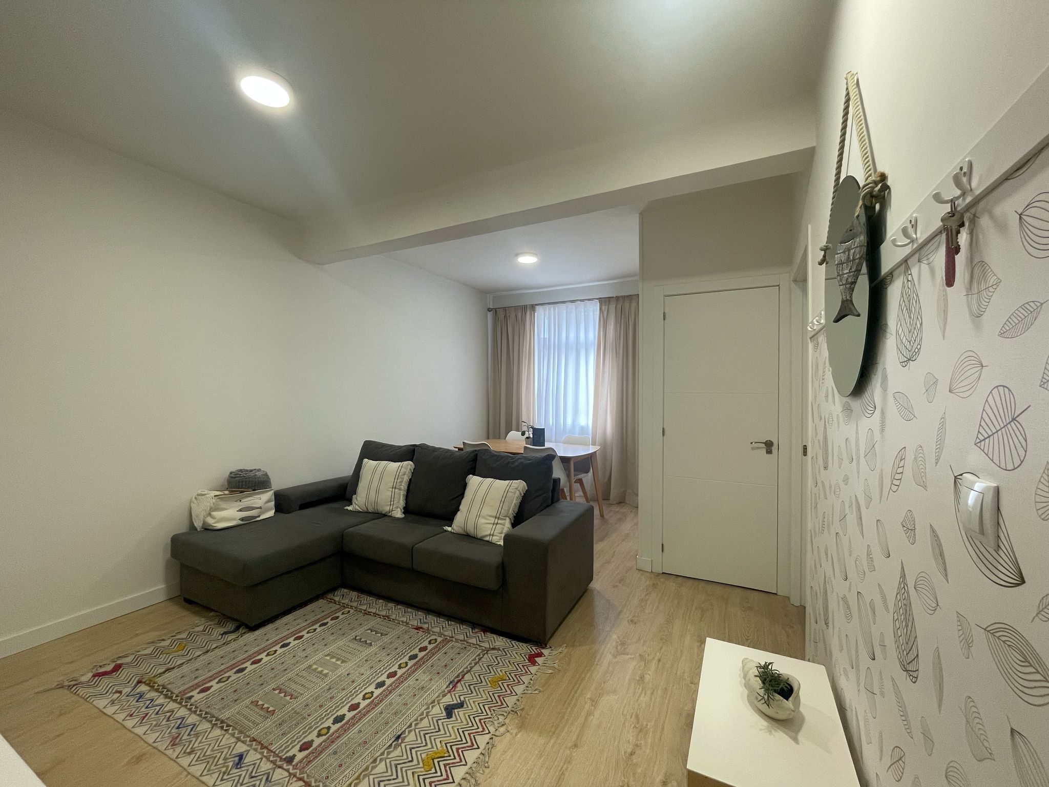 A modern living room with a sectional sofa, a patterned rug, and a dining area in the background.