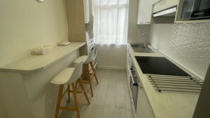 A compact kitchen with a sink, stove, and bar stools. - Airtegal Black Sands (Cedeira)