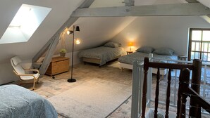 A cozy attic bedroom with a sloped ceiling, a skylight, a bed, a chair, a small table, and a lamp.