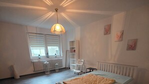 Een slaapkamer met een bed, een radiator, een raam met zonwering, een staande lamp en een radiatorombouw op de vloer.