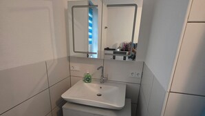 Een kleine badkamer met een wit wastafel, een spiegel en een afvalbak.