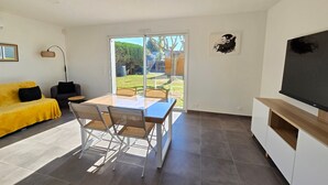 Ein modernes Wohnzimmer mit einem gelben Sofa, einem Esstisch mit Stühlen, einem Fernseher und einer Glastür zum Garten.