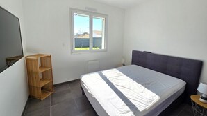 Ein Schlafzimmer mit einem Bett, einem Fenster, einem Nachttisch und einem an der Wand befestigten Regal.