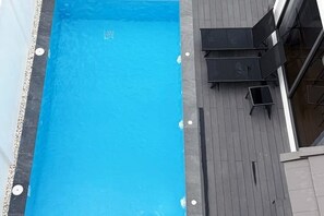 En swimmingpool med træterrasse og sort udendørs møbler.