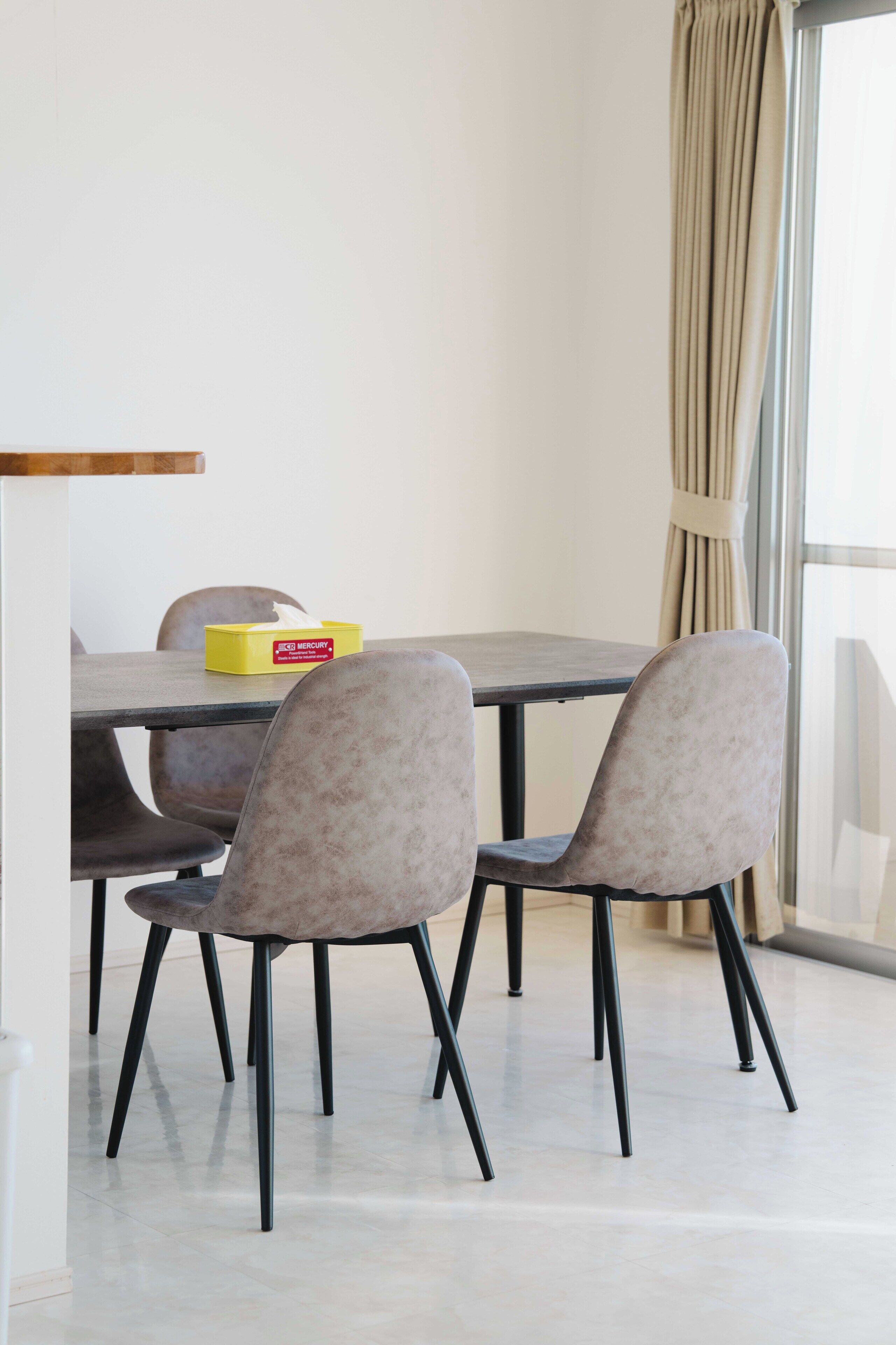 A dining area with a table and chairs, a yellow box on the table, and a window with curtains.