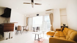 A modern living room with a sofa, a dining table, chairs, a kitchen area, and a balcony with a view. - LoveOkinawa-Nakadomari (Onna)