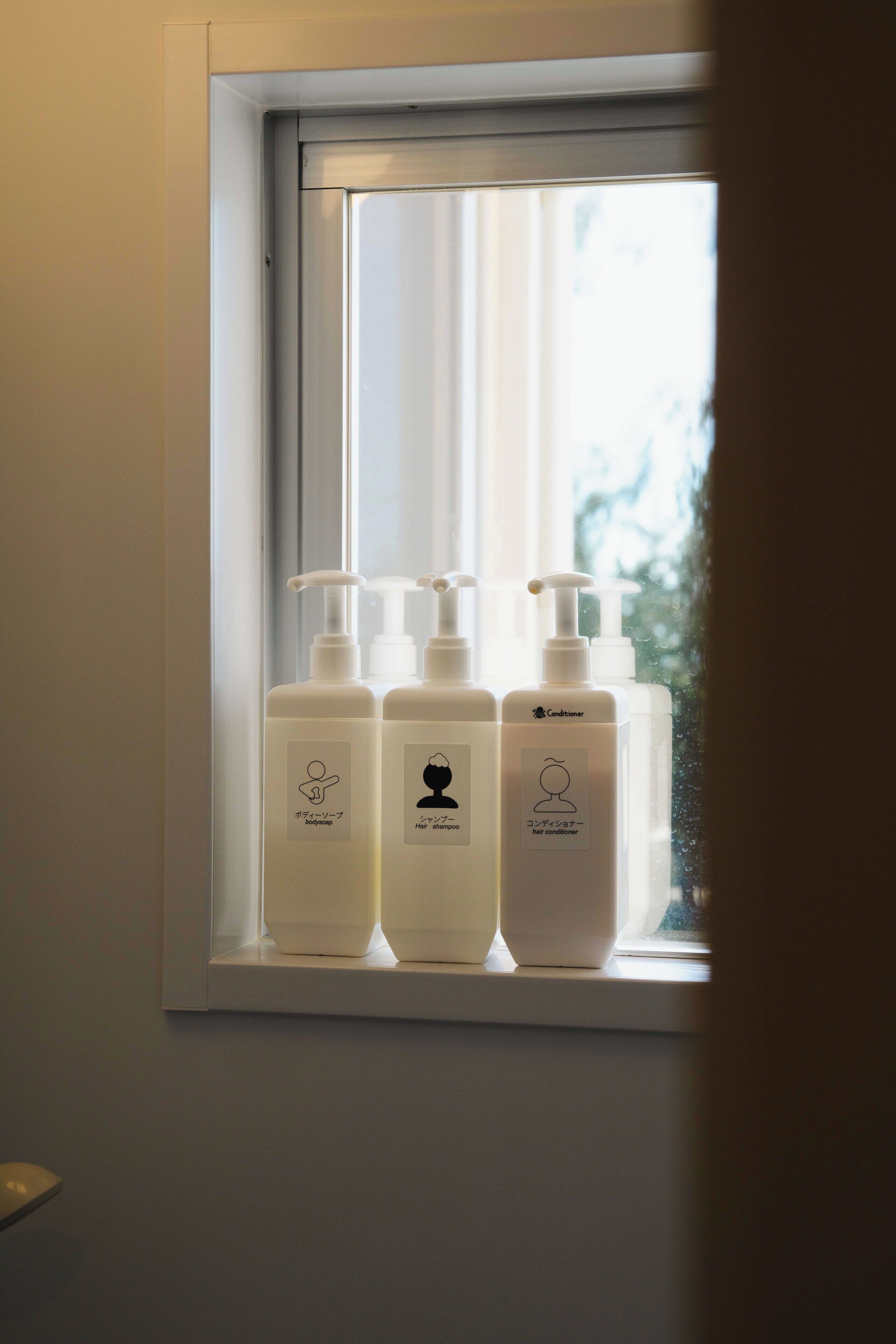 Three white bottles of hair care products on a shelf by a window.