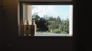 A window with three bottles of lotion on the sill, a view of trees and a clear sky. - LoveOkinawa-Nakadomari (Onna)