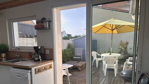 Une cuisine équipée d’un lave-vaisselle, d’une machine à café et d’une fenêtre donnant sur une terrasse avec une table et des chaises.