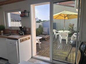 Una cocina con lavavajillas, cafetera y ventana con vistas a un patio con mesa y sillas.