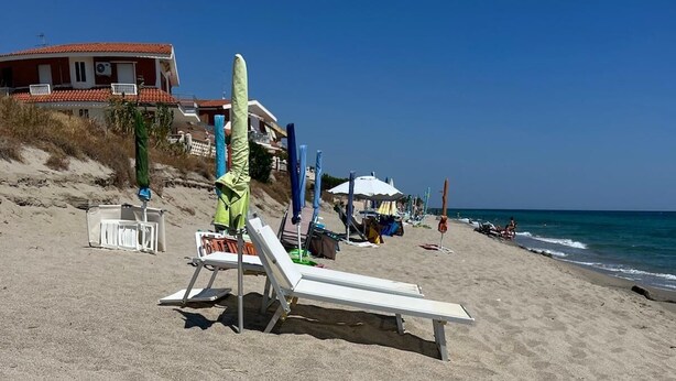A beach with a white lounge chair, a green umbrella, and a white beach chair.