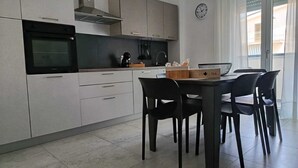 A modern kitchen with a built-in oven, a coffee machine, and a dining table with chairs.