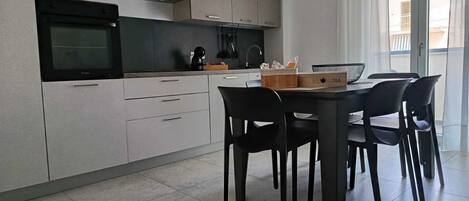 A modern kitchen with a built-in oven, a coffee machine, and a dining table with chairs.