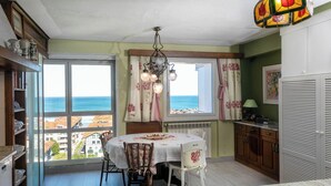 A dining area with a table set for two, a chandelier, and a view of the sea through large windows.
