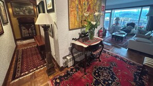 A spacious living room with a large window, a fireplace, and a red patterned rug.