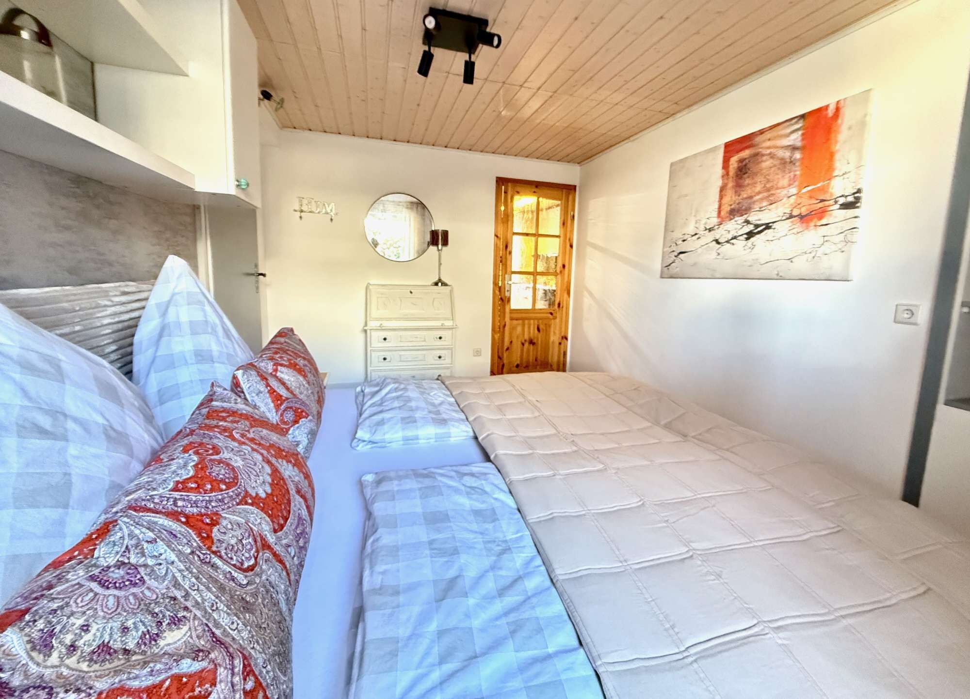 A bedroom with two beds, a wooden ceiling, a mirror, a door, and a painting on the wall.