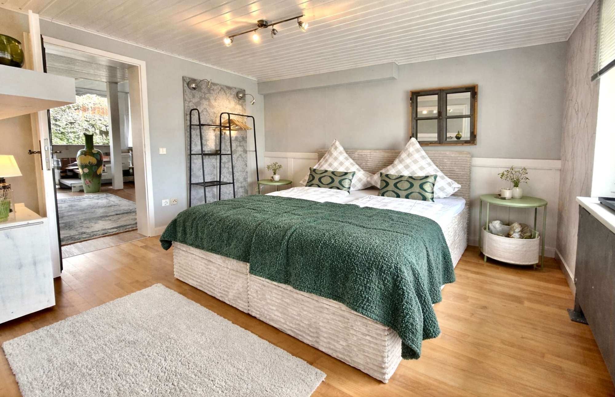 A bedroom with a bed, bedside tables, a nightstand, a mirror, and a window.