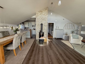 Een ruime loft met een hoge plafond, een centraal geplaatste open haard, een eethoek met een houten tafel en stoelen, en een keuken met moderne apparatuur.