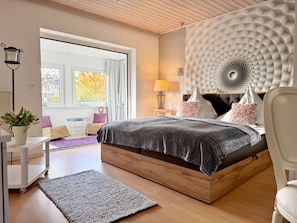 Een moderne slaapkamer met een groot bed, een houten hoofdbord, een nachtkastje met een lamp en uitzicht op de omgeving.