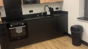 A compact kitchen with dark cabinets, a microwave, a stove, and a trash bin. - Luxury and Spacious 1BR Flat Sleeps 4 with Private Patio I Excellent Location (London)