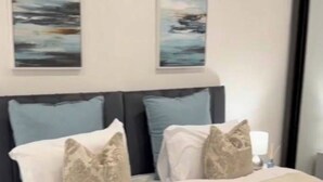A neatly made bed with a rolled towel, a headboard with multiple pillows, and two abstract paintings on the wall. - Luxury and Spacious 1BR Flat Sleeps 4 with Private Patio I Excellent Location (London)