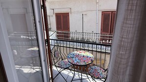 A balcony with a table and chairs, a view of buildings, and a window with a curtain. - Sicilian Luxury for Families, 3 Minutes from the Sea and the UNESCO Cathedral. (Cefalù)