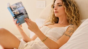 A person lying on a bed reading a book in a room with a wall-mounted light fixture. - Sicilian Luxury for Families, 3 Minutes from the Sea and the UNESCO Cathedral. (Cefalù)
