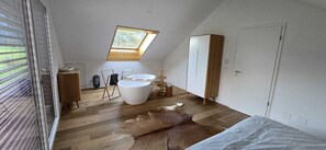 Une chambre avec une lucarne, une grande baignoire, un plancher en bois et un tapis en peau de vache.