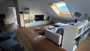 A modern living room with a sloped ceiling, a skylight, a grey sofa, a coffee table, and a dog lying on the floor. - Apartment/flat for rent in Walenstadt (Walenstadt)