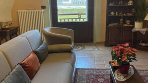 Tunnelmallinen olohuone, jossa on sohva, pieni pöytä, jossa on kasvi, kirjahylly ja näkymä ovesta.