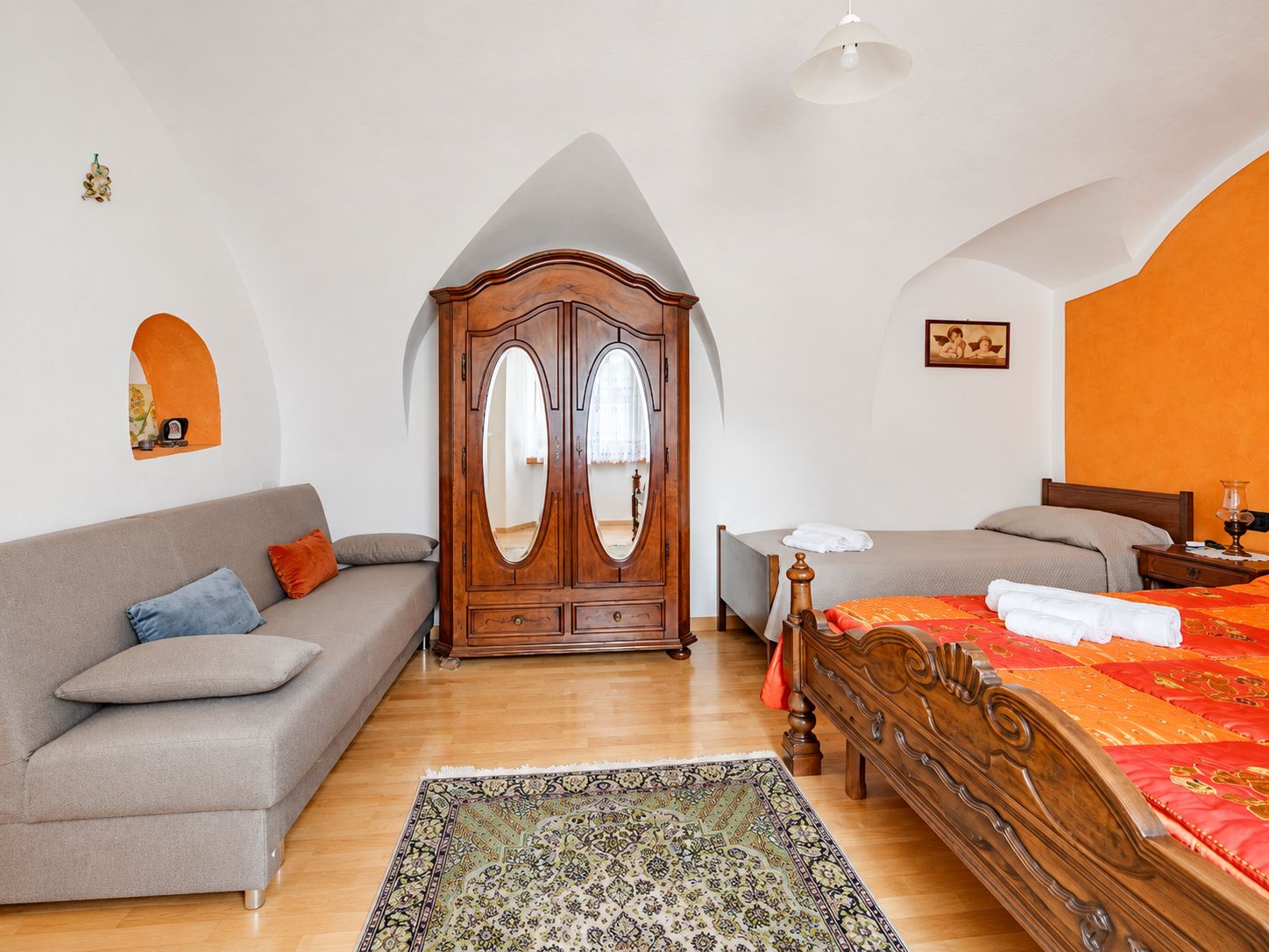 Ein Schlafzimmer mit einem Holzschrank, einer Couch, einem Bett mit roter Bettdecke und einem gemusterten Teppich.