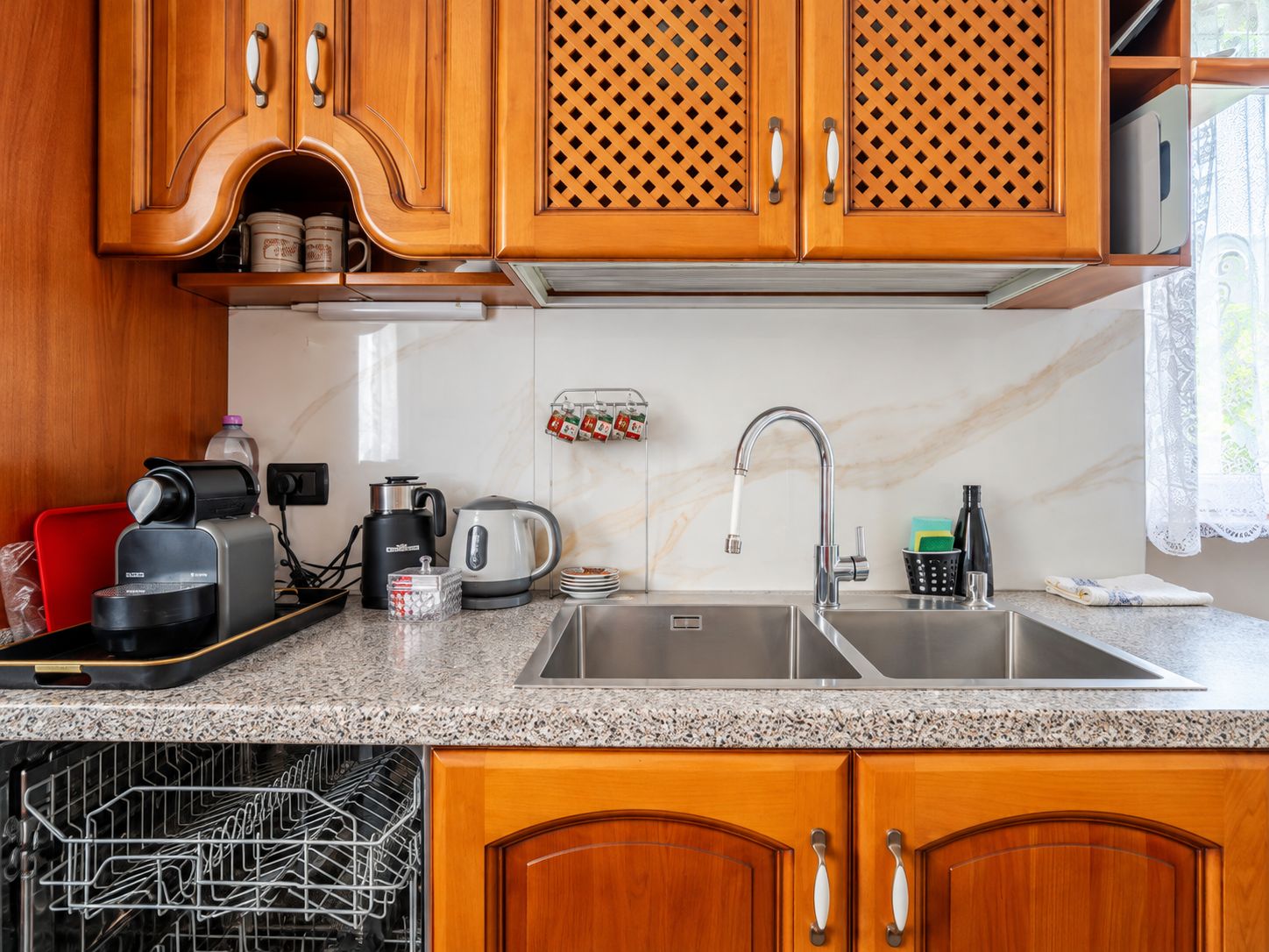 A kitchen with wooden cabinets, a stainless steel sink, a coffee maker, a kettle, and a dish drying rack.