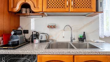 A kitchen with wooden cabinets, a stainless steel sink, a coffee maker, a kettle, and a dish drying rack.