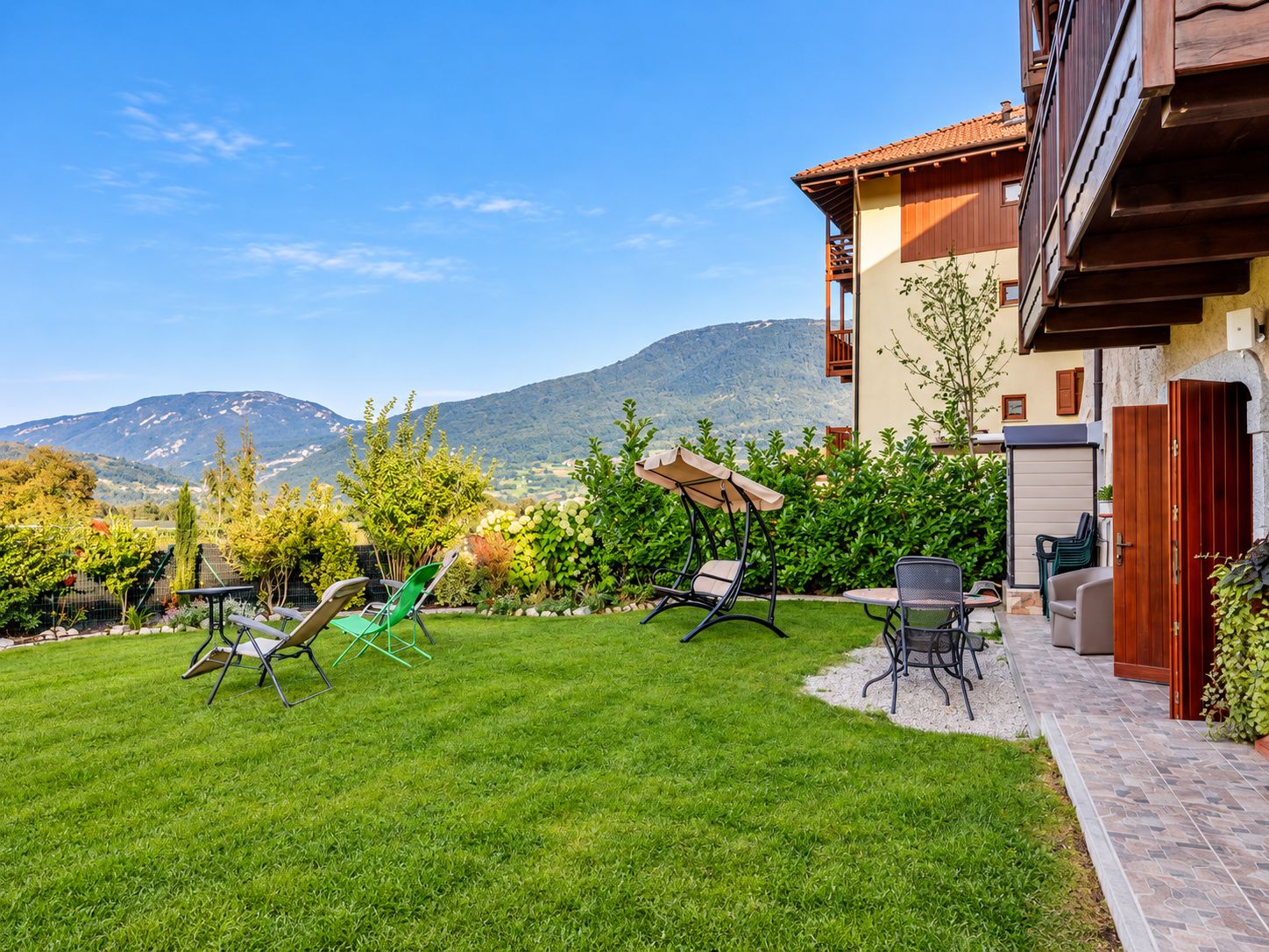A well-maintained garden with a patio area, outdoor furniture, and a view of mountains in the background.