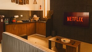 A cozy living room with a sofa, a coffee table, and a TV displaying "NETFLIX". - Arambol Bliss Hote Apartments (Arambol)