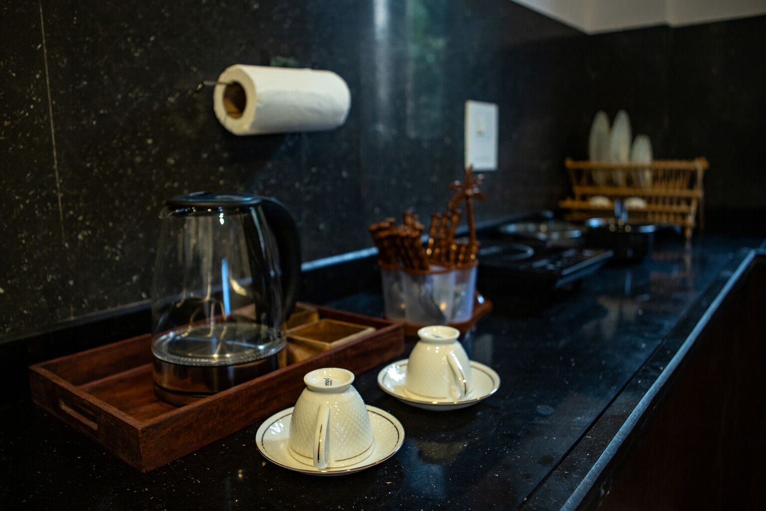 Una encimera de cocina con una cafetera, dos tazas de té y un rollo de toallas de papel.