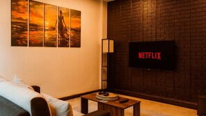 A cozy living room with a sofa, a coffee table, and a flat-screen TV mounted on a brick wall. - Arambol Bliss Hote Apartments (Arambol)