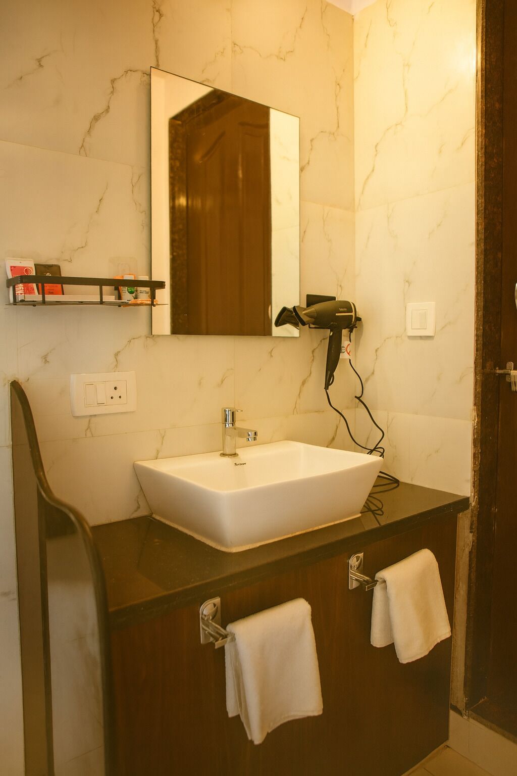 A bathroom with a white sink, a mirror, a hairdryer, and two towels hanging on towel bars.
