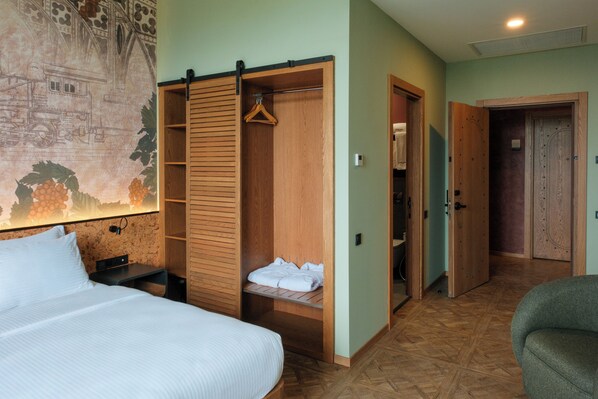 A hotel room with a bed, a wooden wardrobe, a hanging coat rack, and a painting on the wall. - The Wine Station (Tsinandali)