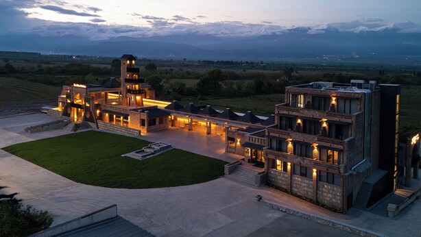 A large, modern building with multiple levels, a central courtyard, and a view of distant mountains. - The Wine Station (Tsinandali)