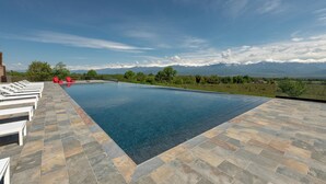 A swimming pool with a view of mountains, lounge chairs, and a clear sky. - The Wine Station (Tsinandali)