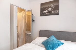 Een slaapkamer met een bed, een douchegordijn, een handdoekrek en een aan de muur hangend beeld van herten.