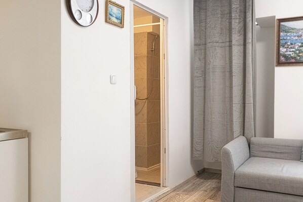 A hallway with a shower, a grey sofa, and a door leading to a bathroom.