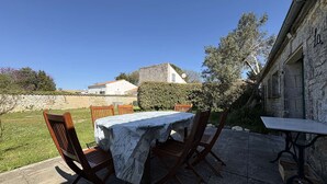 Eine Terrasse im Freien mit Tisch und Stühlen, einer Steinmauer und Blick auf ein Gebäude im Hintergrund.