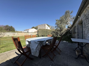 Un patio esterno con tavolo e sedie, un muro in pietra e vista su un edificio sullo sfondo.
